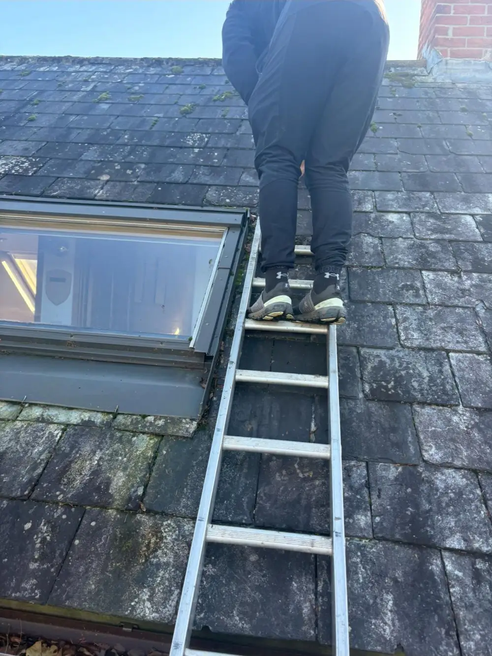 Roofer on a roof ladder beside a roof window on a slate roof